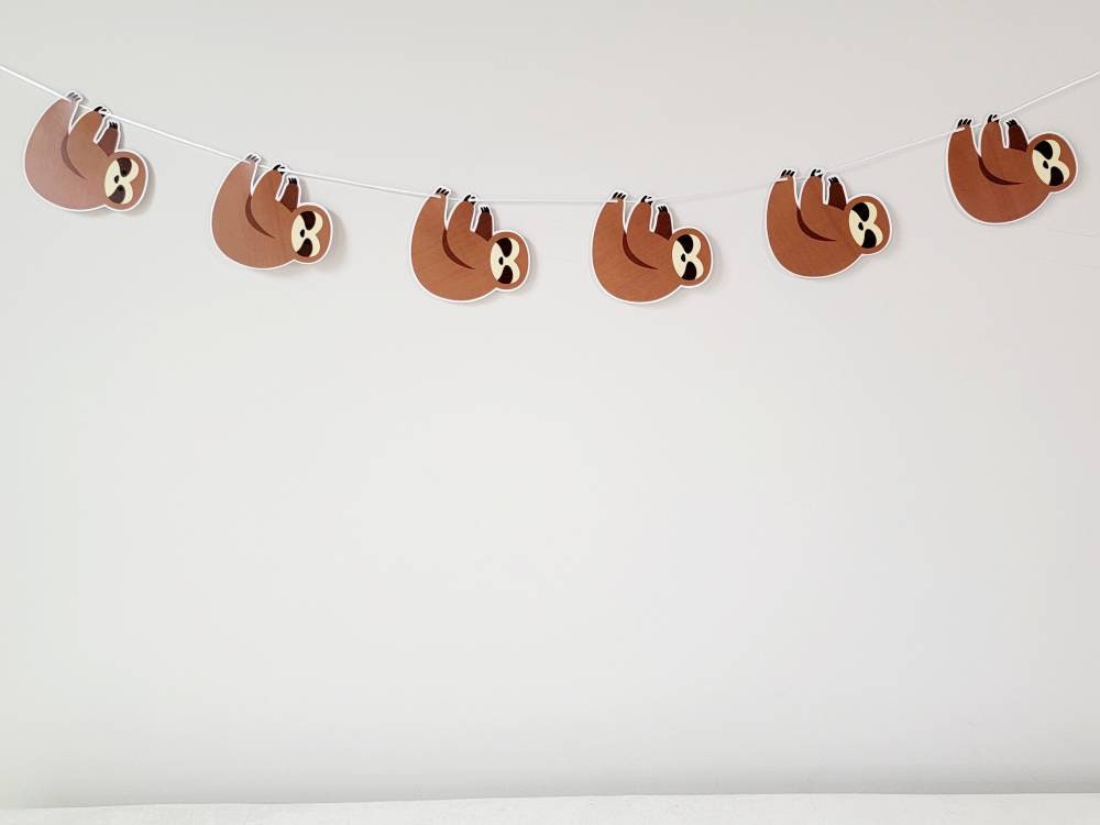 May include: A brown sloth garland with five sloths hanging from a white string. The sloths are facing to the right and have black eyes and noses.