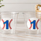May include: Two clear plastic cups with a baseball-themed design. Each cup features a white circle with a blue number 1 and red baseball stitching. The cups are on a light-colored wooden surface.
