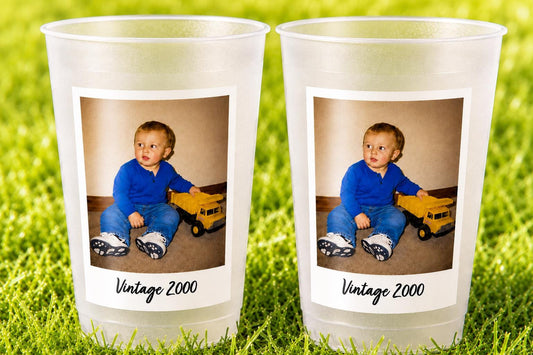 May include: Two frosted plastic cups featuring a rectangular photo print of a toddler wearing a blue long-sleeve shirt and blue jeans, sitting next to a yellow toy dump truck. Below the photo, the text Vintage 2000 is printed in black.